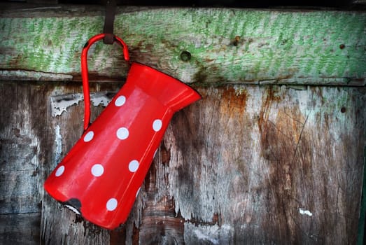 Vintage red jug hanging on rustic wooden wall