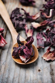Spoon of dried hibiscus tea on wooden background
