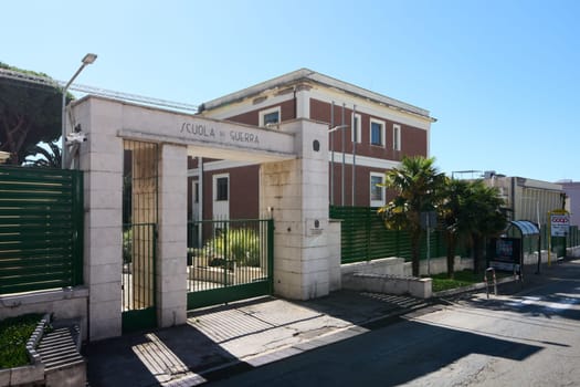 Civitavecchia. Italy - January 26, 2025: Main gate of the Italian War School in Civitavecchia, Italy, with a sign Scuola di Guerra, green fence, and a red brick building in the background.