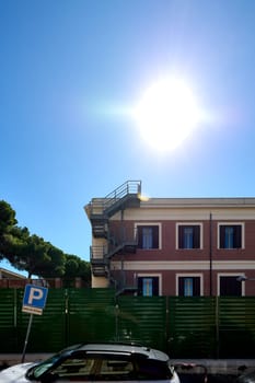 A historic two-story building in Civitavecchia, Italy, featuring a prominent external metal staircase. The structure has a classic architectural style with multiple windows.