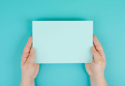 Woman holds a blank sheet of paper, blue colored background, empty copy space for text, minimalism