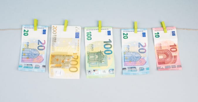Money is hanging on a washing line, grey background, copy space, Euro banknotes, drying after laundry, european currency