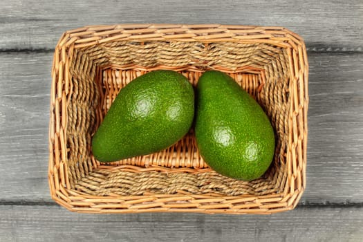 Table top view - two whole avocado pears in rectangular basket.