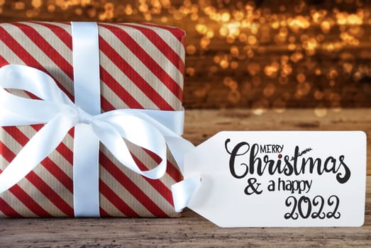 One Christmas Gift With Label With English Calligraphy Merry Christmas And A Happy 2022. Wrapping Paper With A Bow And Lights In Background