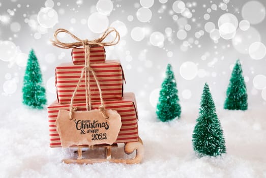 Sled With Christmas Gift And Label With English Calligraphy Merry Christmas And A Happy 2022. Snow With Christmas Tree And Gray Sparkling Background