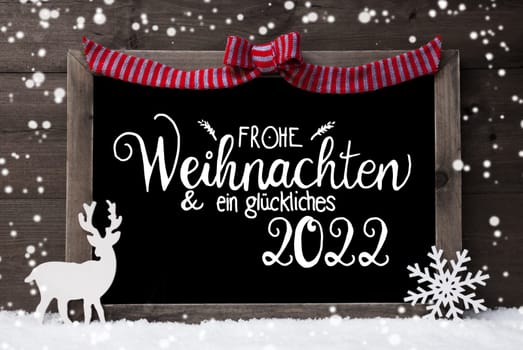 Chalkboard With German Calligraphy Frohe Weihnachten Und Ein Glueckliches 2022 Means Merry Christmas And A Happy 2022. Decoration Like Deer And Bow. Gray Wooden Background With Snow And Snowflakes