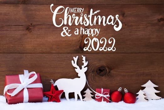 English Calligraphy Merry Christmas And A Happy 2022. Red Christmas Decoration Like Tree, Gift, Ball And Reindeer. Wooden Background With Snow