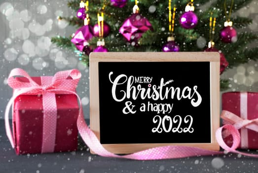 Blackboard With Egnlish Calligraphy Merry Christmas And Happy 2022. Christmas Tree With Purple Ball Ornament, Pink Gift And Bokeh Effect And Snowflakes