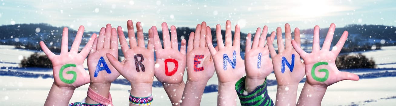 Children Hands Building Colorful English Word Gardening. Snowy Winter Background With Snowflakes