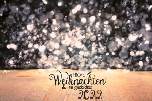 German Calligraphy Frohe Weihnachten Und Ein Glueckliches 2022 Means Merry Christmas And Happy 2022. Black Christmas Background With Sparkling Lights And Wood