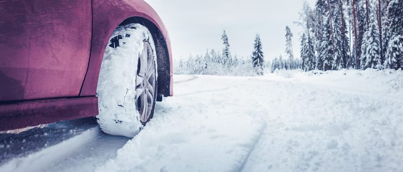 Panoramic view of the red car on the snowy road. Concept of the danger of driving on a winter road and travelling by auto in Christmas holidays.