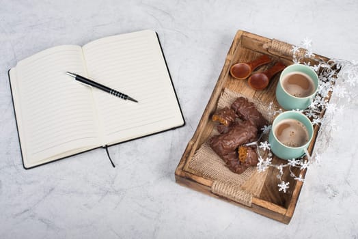 Coffee cups and chocolate coated gingerbread in a wooden basket, christmas season empty copy space, book with a pen