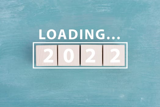 2022 is standing in white colored letters on wooden cubes, the word loading is standing above, blue background