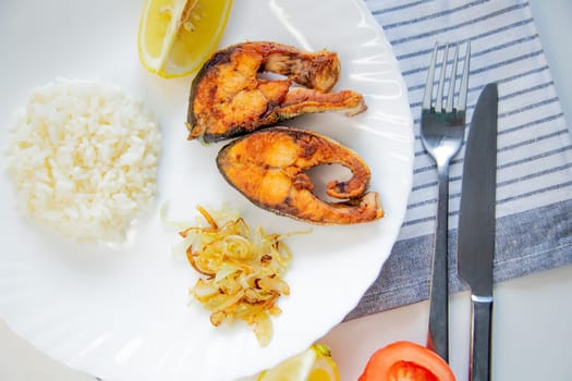 Fried fish with onions, rice and lemon lies on a plate, on a waffle towel and cutlery on a white background. High quality photo