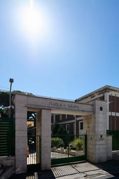 Civitavecchia. Italy - January 26, 2025: The entrance gate of the Italian War School in Civitavecchia, with a sign, green metal fence, and a red brick building, under a bright sunny sky.