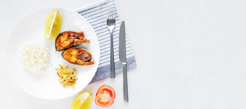 Fried fish with onions, rice and lemon lies on a plate, on a waffle towel and cutlery on a white background. High quality photo
