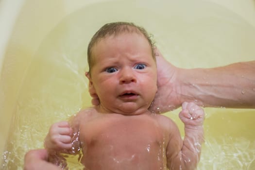 A newborn baby is bathing in a bath for the first time, his hand is holding his head, the baby is scared. High quality photo