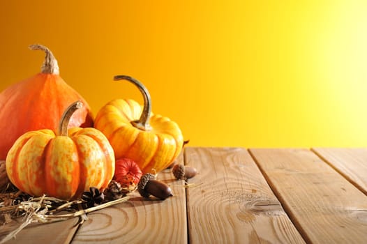 Three pumpkins on old wooden boards against a brown background with light from the side.