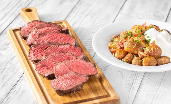 Perfectly sliced steak with golden potatoes, crispy bacon, gooey cheddar, and fresh onions