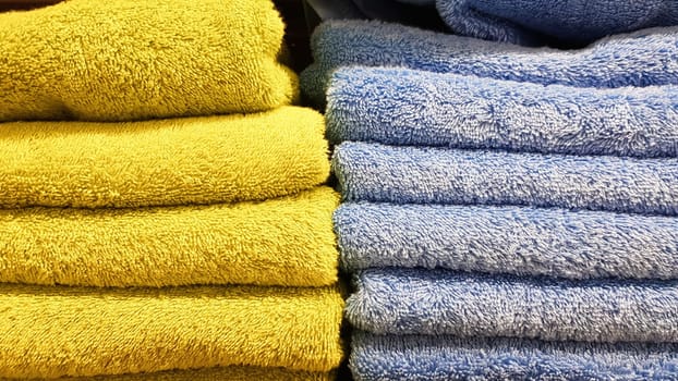 Stacks of fluffy bath towels of various colors in a store window. Terry cotton towels in a stack on the shelves of a supermarket