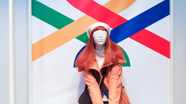 one woman mannequin in luxurious winter or autumn clothes in a shop window. A red-haired female mannequin demonstrates a casual collection of clothing. Brown coat