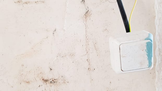 one white light switch in paint and putty is temporarily hanging on a black wire during repair against the background of an unfinished wall. open the wires
