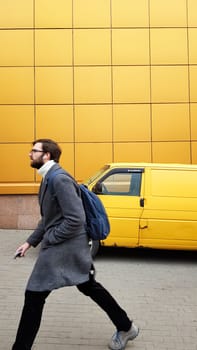 Ukraine, Kiev - February 25, 2020: a mature male businessman in a hurry to meet or work in a gray coat on a yellow background. Casual style. fashionable man with a beard. Male fashion model