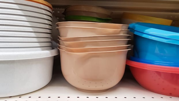 Multi-colored plastic containers of different shapes and sizes with and without lids, stacked in a pile on a store window. Sale of boxes for storage and cleaning. Modern kitchen utensils.