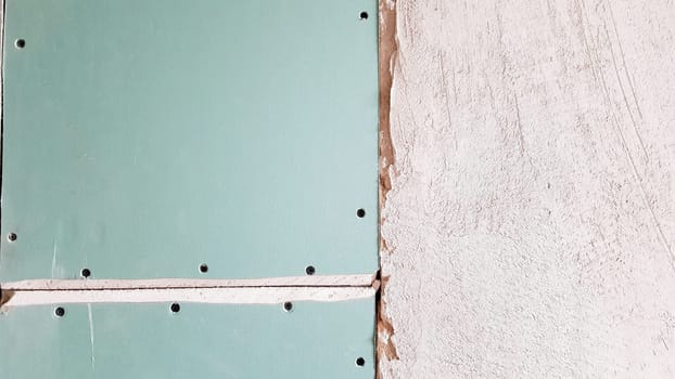 Unfinished wall in a building under construction made of plasterboard. Part of the wall is sheathed with drywall. Drywall is bolted to the wall in anticipation of plaster