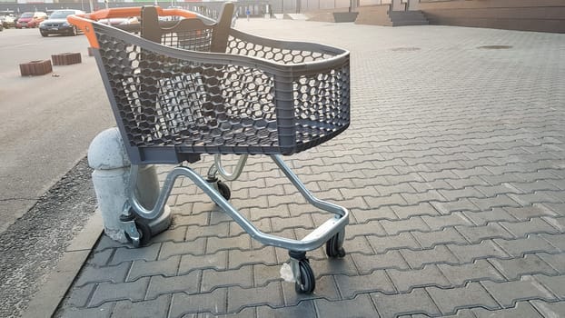 Empty grocery cart outdoor near the supermarket. Loneliness, cart isolation, quarantine, coronavirus. one empty plastic basket on wheels with yellow plastic parts left on the sidewalk near the store