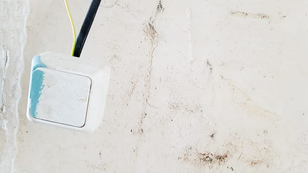 one white light switch in paint and putty is temporarily hanging on a black wire during repair against the background of an unfinished wall. open the wires