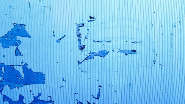 Uneven wavy plastic surface with the remains of flaky film and paper. Abstract obsolete blue background. Copy space, design. Grain blue paint wall background or texture.