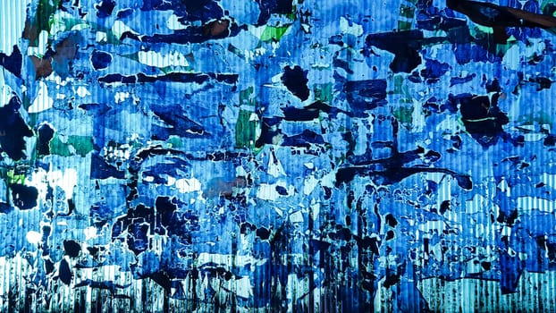 Uneven wavy plastic surface with the remains of flaky film and paper. Abstract obsolete blue background. Copy space, design. Grain blue paint wall background or texture.