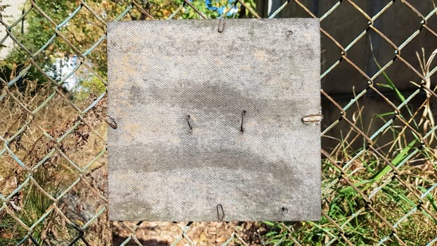 Old cracked square wooden plate on an old metal mesh. Place for your text or logo. Copy space.