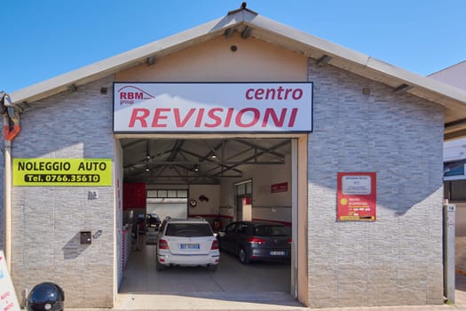 Civitavecchia. Italy - January 26, 2025: Automotive service center exterior with visible centro REVISIONI, RBM group, and NOLEGGIO AUTO signage. Two cars inside the garage.