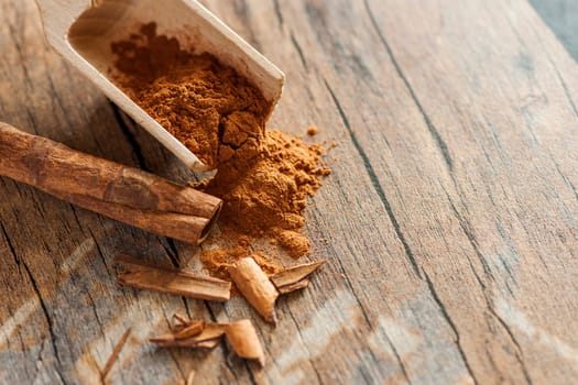 Close-up, elevated view of a wooden scoop with cinnamon powder and cinnamon fragments on an old wooden surface in an elevated view at aperture F / 5.6
