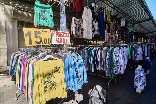 Civitavecchia, Italy - January 26, 2025: A street market stall displaying a variety of colorful clothing items. The display includes shirts, dresses, and jackets with a sign with the price of 15 euros