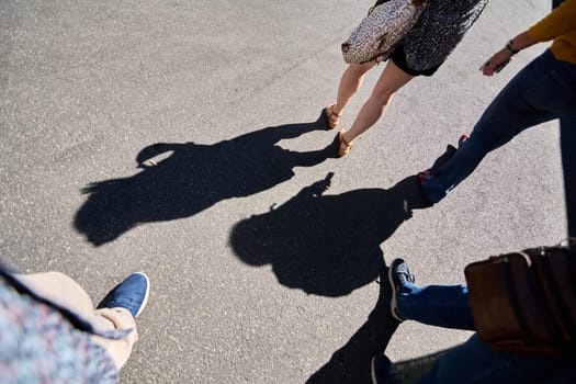 Civitavecchia. Italy - January 26, 2025: Casual urban stroll. Four people walking on a paved surface, casting long shadows. The image captures diverse clothing and footwear styles in an urban environment.