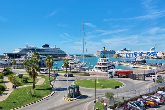 Civitavecchia. Italy - January 26, 2025: The busy port of Civitavecchia with large cruise ships, yachts, and a roundabout surrounded by palm trees. A picturesque scene for travel and maritime themes.