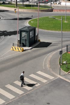 Civitavecchia. Italy - January 27, 2025: A pedestrian crossing near a small green guardhouse and traffic barriers at a roundabout in Civitavecchia. Concept: urban security and transportation scene.