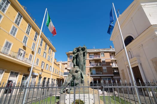 Civitavecchia, Italy - January 27, 2025: War memorial statue in Civitavecchia, Italy, dedicated to fallen soldiers. It features a central figure with outstretched arms, flanked by Italian and EU flags