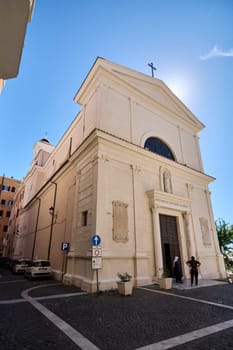 Civitavecchia, Italy - January 27, 2025: Civitavecchia Church with a sunlit facade. The image shows parked cars and a clear blue sky, highlighting the beauty of Italian architecture and culture.