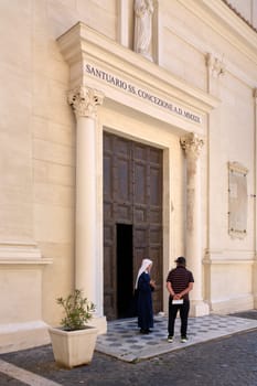 Civitavecchia. Italy - January 27, 2025: Entrance to the Church of the Japanese Martyrs in Civitavecchia, Italy. The facade features ornate columns, a statue, and an inscription above the door. Two individuals, one in a dark habit, stand near the entrance.