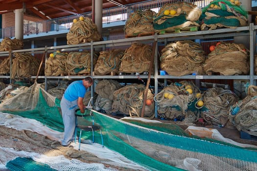 Civitavecchia, Italy - January 31, 2025: A man repairs fishing nets in a well-organized warehouse. This image captures the intricate process and essential maintenance work
