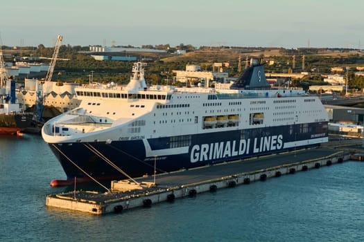 Civitavecchia. Italy - February 06, 2025: Grimaldi Lines ferry CRUISE BARCELONA docked at Civitavecchia port with industrial background, showcasing the scale of maritime transport.
