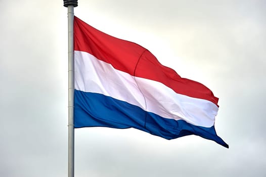 The flag of the Netherlands hangs on a metal flagpole. High quality photo
