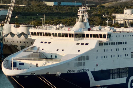 Civitavecchia. Italy - February 06, 2025: The large cruise ship CRUISE BARCELONA docked in an industrial port with storage tanks and crane visible. Perfect for travel and marine architecture.