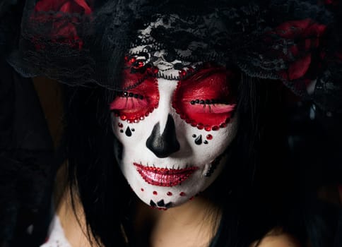 portrait of a beautiful woman with closed eyes and a sugar skull makeup with a wreath of flowers on her head, close up