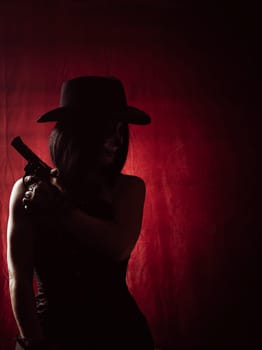 woman in corset and black hat holding revolver on red background, silhouette