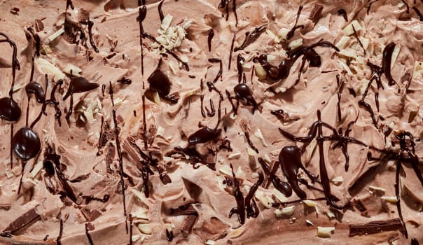 Textured chocolate ice cream surface with drizzled sauce and chopped almond and hazelnuts in a close up full frame background
